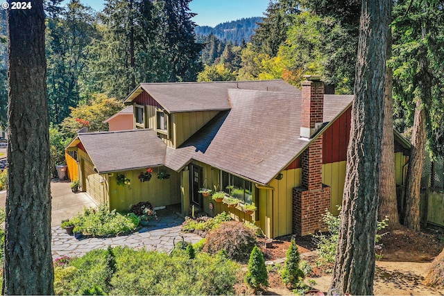 view of front of property featuring a chimney, concrete driveway, a view of trees, and board and batten siding