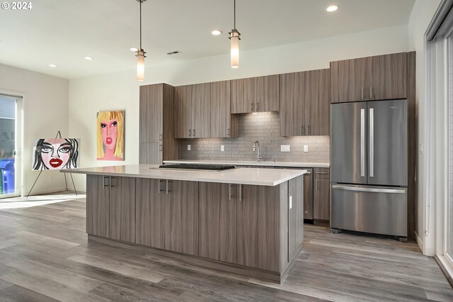 kitchen with light wood-type flooring, stainless steel refrigerator, decorative backsplash, and hanging light fixtures