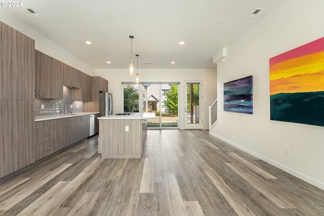 kitchen featuring backsplash, stainless steel appliances, decorative light fixtures, wood-type flooring, and a kitchen island