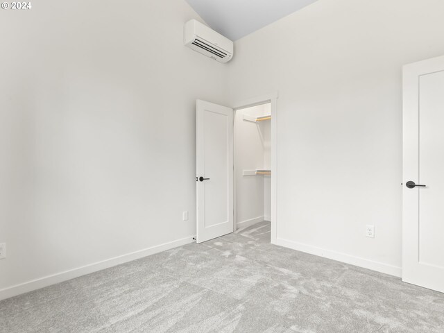 unfurnished bedroom featuring a walk in closet, carpet floors, and a wall mounted AC