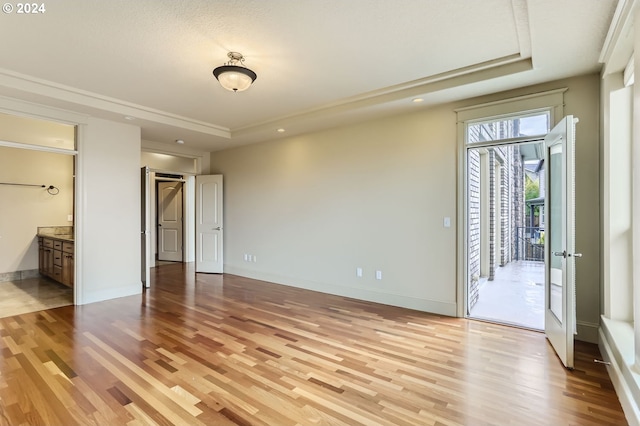 unfurnished bedroom featuring a tray ceiling, ensuite bath, access to exterior, and light wood-type flooring