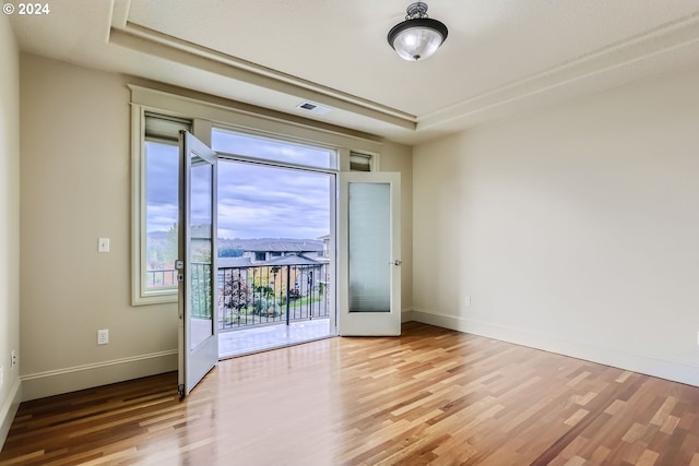 empty room with french doors, light wood-type flooring, and a raised ceiling