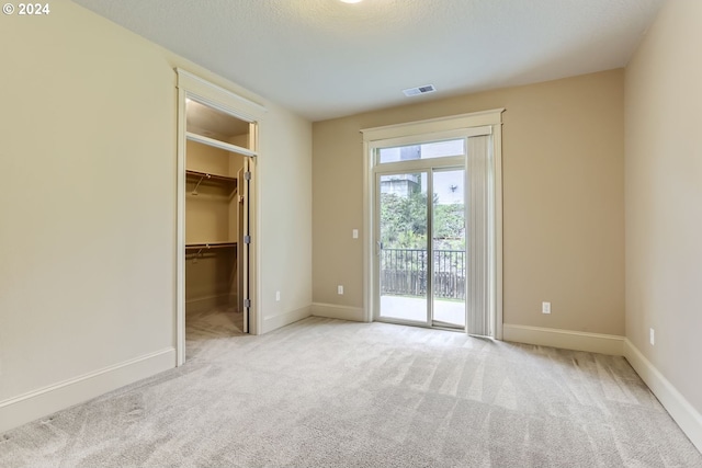 unfurnished bedroom with light carpet, a walk in closet, access to exterior, a textured ceiling, and a closet