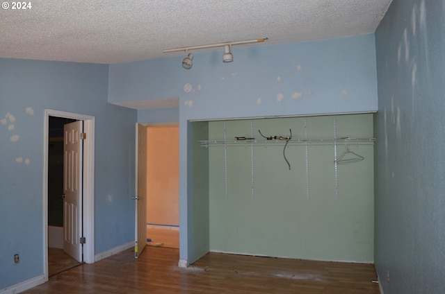 unfurnished bedroom with a closet, track lighting, hardwood / wood-style flooring, and a textured ceiling