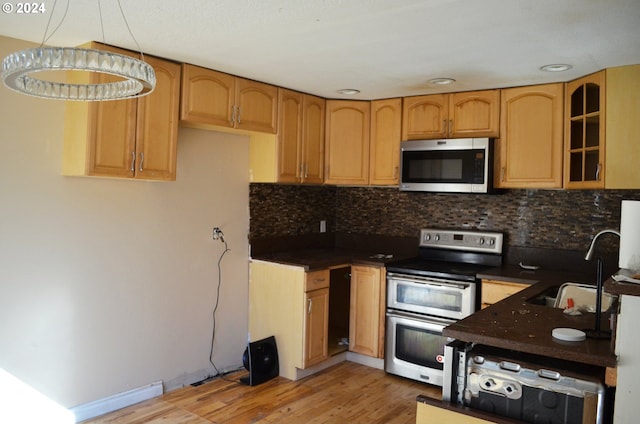 kitchen with hanging light fixtures, sink, light hardwood / wood-style flooring, backsplash, and stainless steel appliances