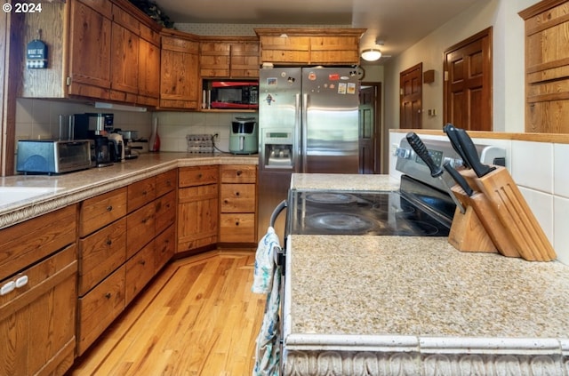 kitchen featuring light hardwood / wood-style floors, stove, stainless steel refrigerator with ice dispenser, tasteful backsplash, and black microwave