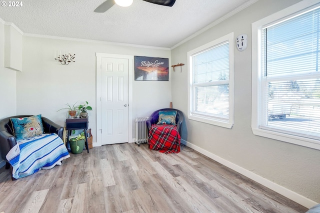 living area featuring light hardwood / wood-style flooring, ceiling fan, crown molding, radiator heating unit, and a textured ceiling