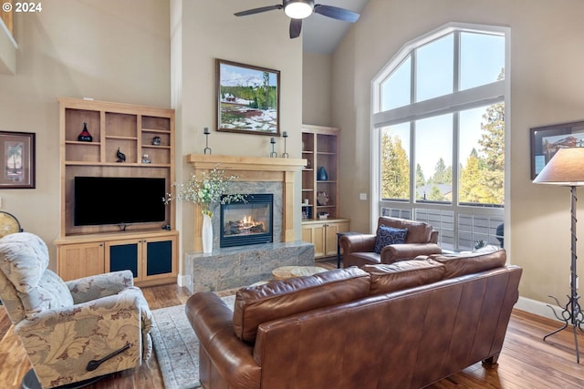 living room with a high end fireplace, high vaulted ceiling, light hardwood / wood-style flooring, and ceiling fan