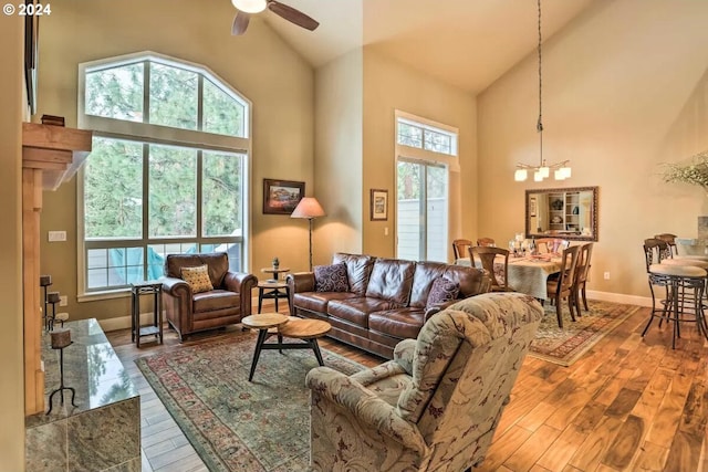 living room with ceiling fan with notable chandelier, hardwood / wood-style flooring, and high vaulted ceiling