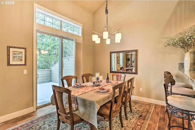 dining space with an inviting chandelier, a towering ceiling, and hardwood / wood-style floors