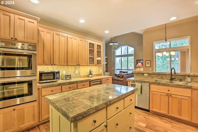 kitchen with ceiling fan, sink, a kitchen island, stainless steel appliances, and light hardwood / wood-style floors