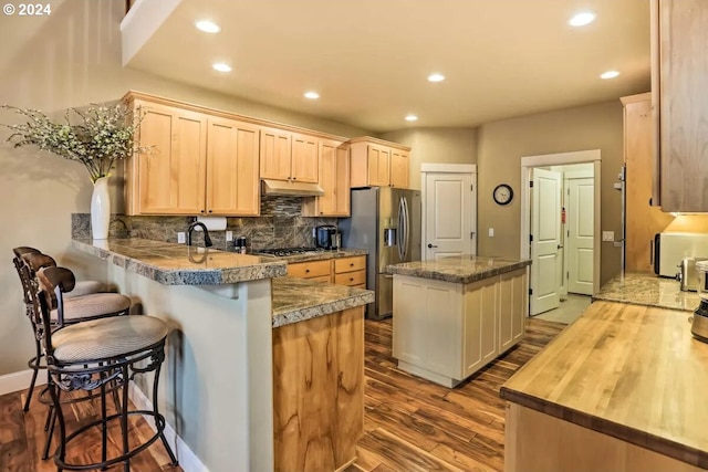 kitchen with kitchen peninsula, appliances with stainless steel finishes, light brown cabinetry, a breakfast bar area, and hardwood / wood-style floors