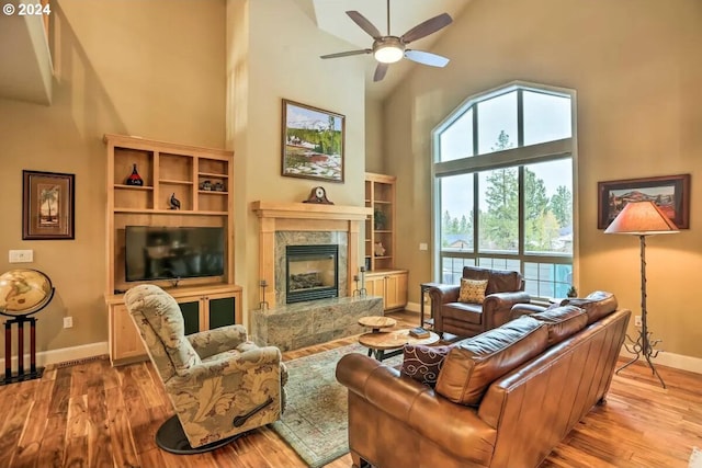 living room featuring light wood-type flooring, high vaulted ceiling, ceiling fan, and a fireplace