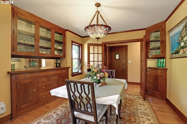 dining space featuring light wood-style floors, a textured ceiling, baseboards, and crown molding