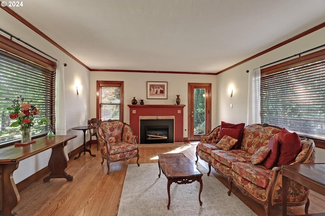 living room with a glass covered fireplace, baseboards, crown molding, and light wood finished floors