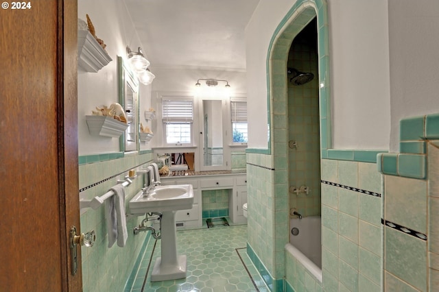 bathroom with a wainscoted wall, tile walls, toilet, tiled shower / bath combo, and tile patterned flooring