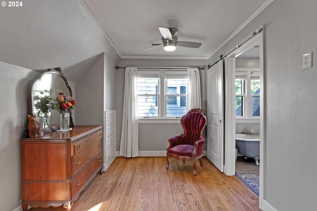 sitting room featuring light wood finished floors, a barn door, baseboards, a ceiling fan, and ornamental molding