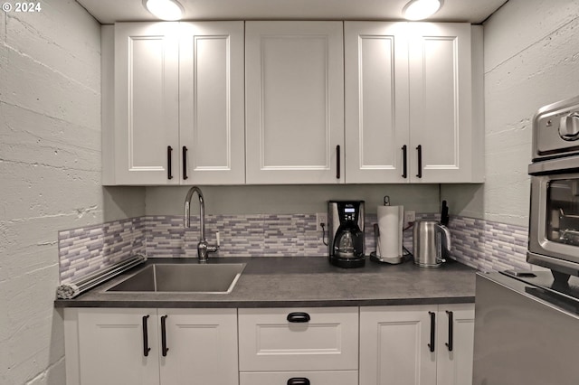 kitchen featuring dark countertops, white cabinetry, backsplash, and a sink