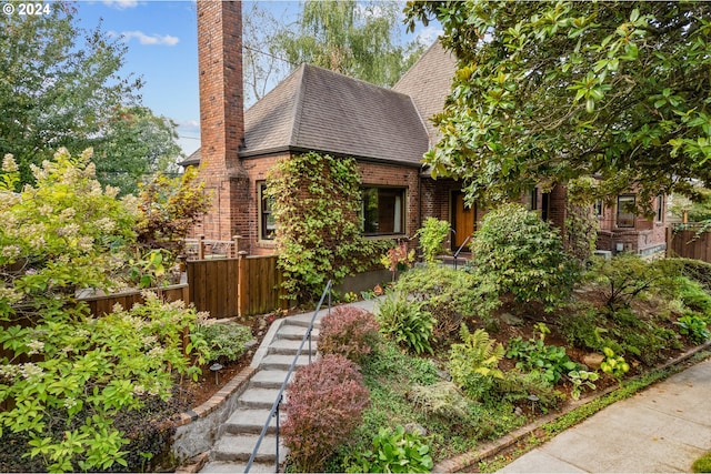 view of front of home with a shingled roof, a chimney, fence, and brick siding