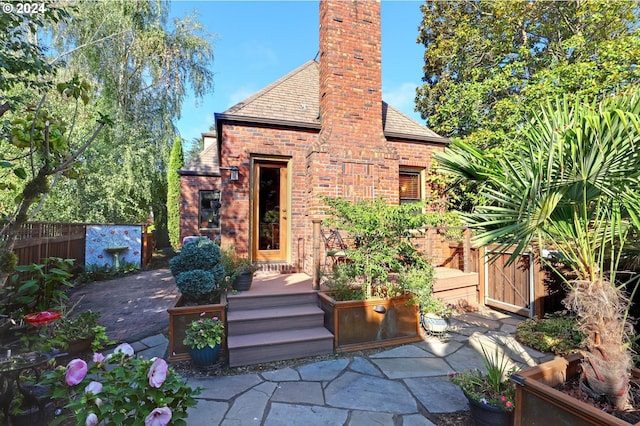 back of property featuring a chimney, fence, a patio area, a high end roof, and brick siding