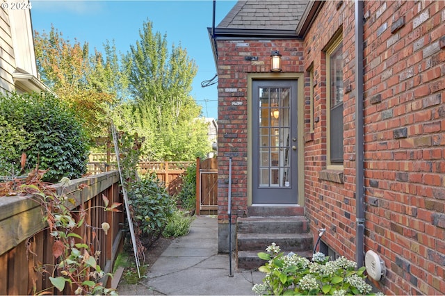 property entrance with brick siding, roof with shingles, and fence