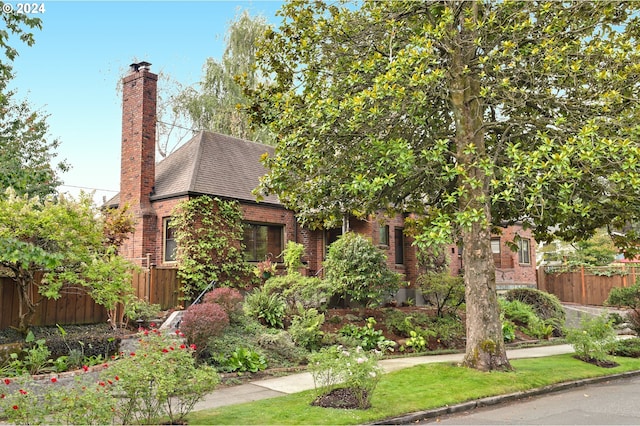 view of front of property with brick siding, a chimney, a shingled roof, and fence