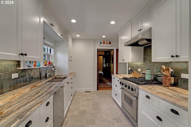 kitchen featuring white cabinets, appliances with stainless steel finishes, light stone counters, under cabinet range hood, and a sink