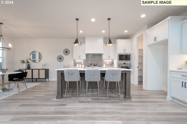 kitchen featuring custom exhaust hood, built in microwave, a center island with sink, and decorative light fixtures