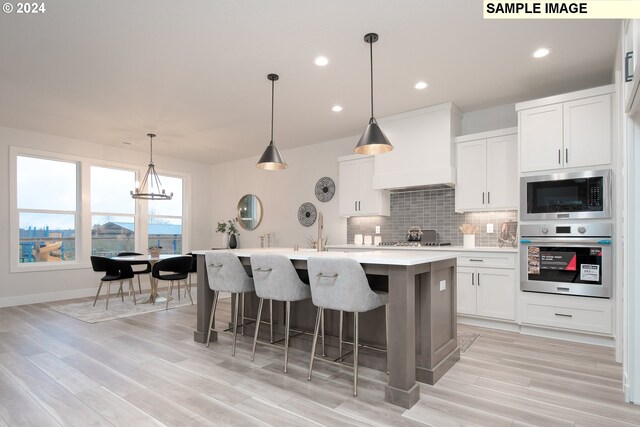 kitchen featuring premium range hood, a kitchen island with sink, backsplash, stainless steel appliances, and light countertops