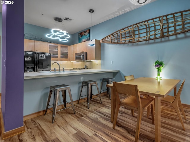 kitchen with hanging light fixtures, black refrigerator with ice dispenser, kitchen peninsula, light hardwood / wood-style floors, and a kitchen bar