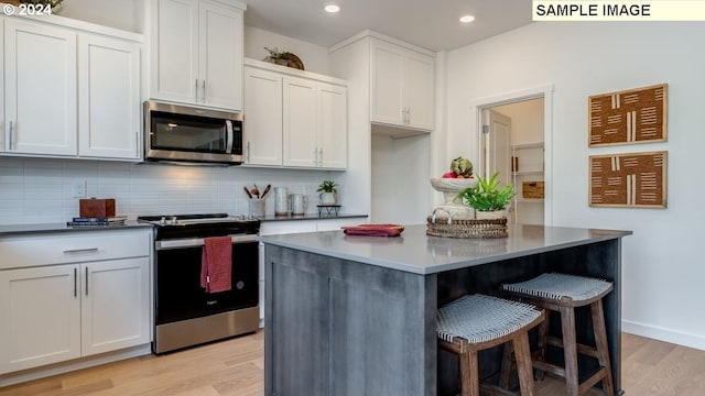 kitchen with white cabinets, a kitchen breakfast bar, appliances with stainless steel finishes, light wood-type flooring, and backsplash