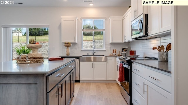 kitchen with range with electric cooktop, white cabinets, stainless steel microwave, light wood-type flooring, and a sink