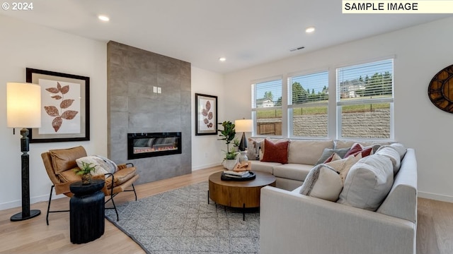 living room featuring a tile fireplace, light wood-style flooring, recessed lighting, visible vents, and baseboards