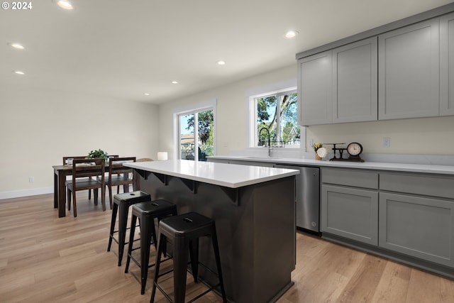 kitchen featuring dishwasher, a kitchen island, a kitchen breakfast bar, light hardwood / wood-style flooring, and gray cabinetry