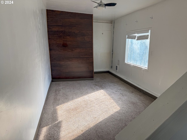 empty room with wood walls, carpet floors, and ceiling fan