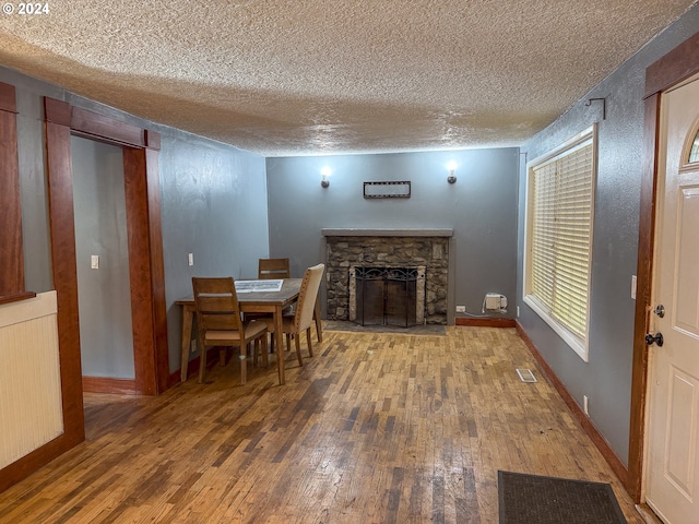 dining space with a textured ceiling, a stone fireplace, wood-type flooring, and radiator heating unit