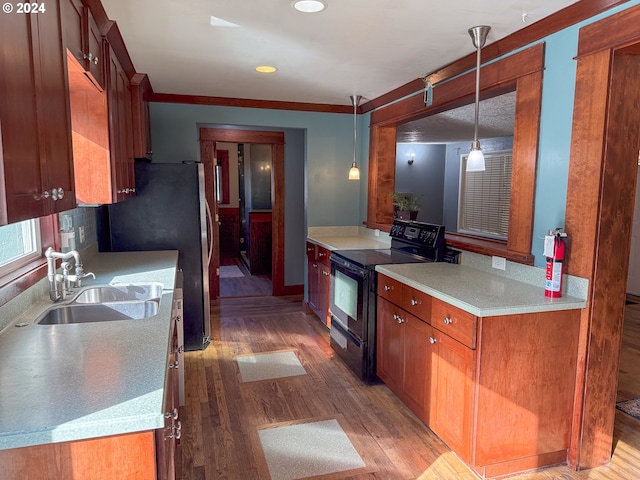 kitchen featuring electric range, wood-type flooring, ornamental molding, pendant lighting, and sink