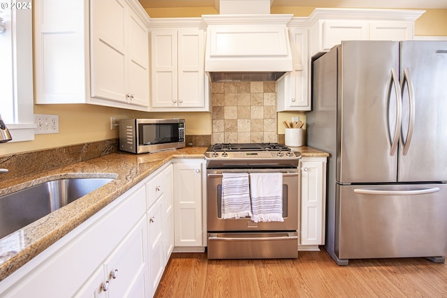 kitchen featuring custom exhaust hood, light hardwood / wood-style floors, white cabinetry, and stainless steel appliances