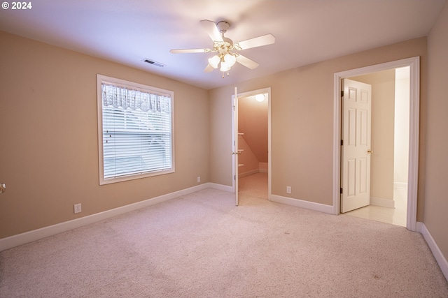 unfurnished bedroom with a closet, a walk in closet, light colored carpet, and ceiling fan