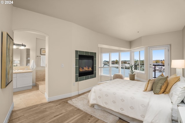 bedroom with arched walkways, connected bathroom, access to exterior, light wood-type flooring, and a fireplace