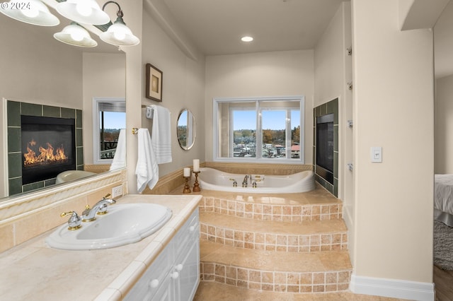 ensuite bathroom featuring a tile fireplace, a garden tub, connected bathroom, and vanity