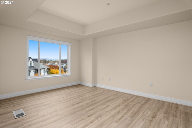 empty room with light wood-type flooring, baseboards, visible vents, and a tray ceiling