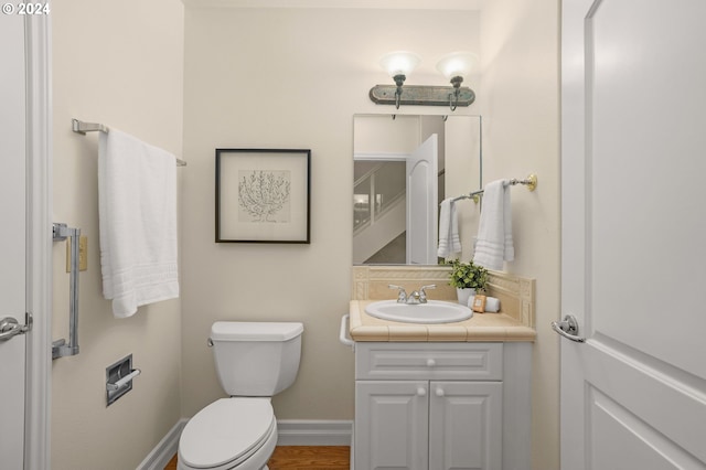 half bath with toilet, baseboards, and vanity