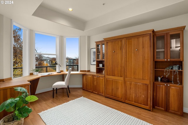 office space with a tray ceiling, built in desk, recessed lighting, light wood-type flooring, and baseboards