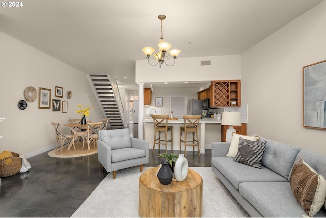 living room with a notable chandelier, concrete floors, baseboards, stairway, and ornate columns