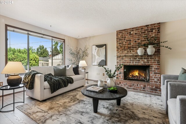 living room featuring a textured ceiling, brick wall, hardwood / wood-style flooring, and a brick fireplace