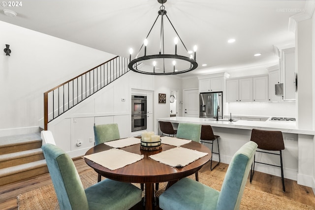 dining space with an inviting chandelier, sink, and light hardwood / wood-style flooring