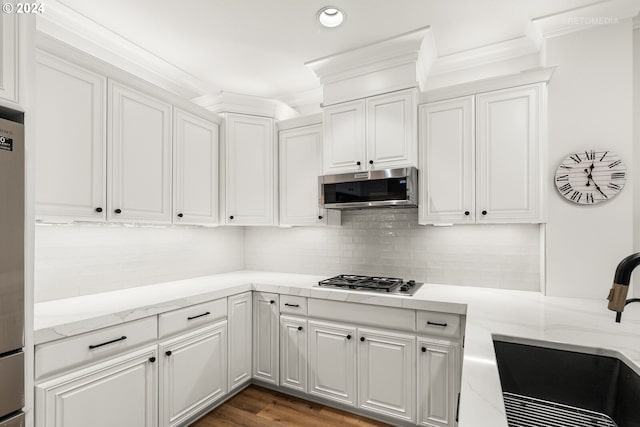 kitchen with sink, crown molding, appliances with stainless steel finishes, white cabinets, and backsplash