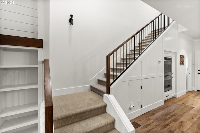 staircase featuring hardwood / wood-style flooring, crown molding, and built in shelves