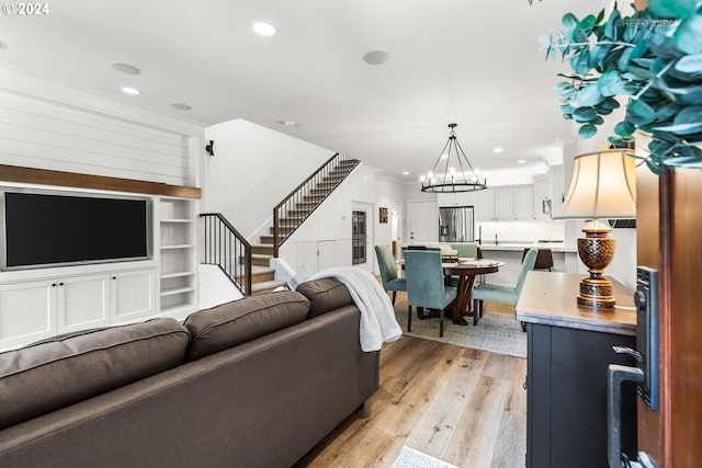 living room featuring built in features, ornamental molding, a notable chandelier, and light wood-type flooring